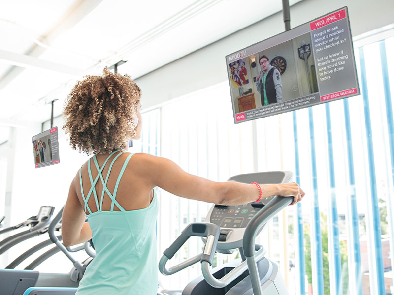 woman working out on treadmill watching tv at apartment gym